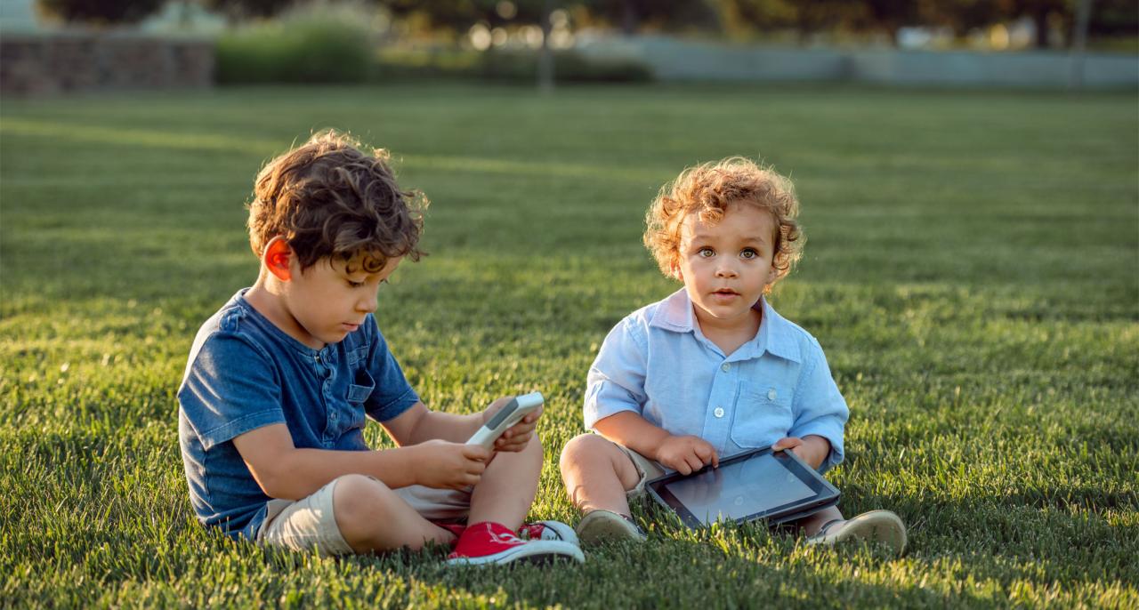 Middle Names for Boys - Two cute little brothers, both boys of color, playing with electronic items at a public park.